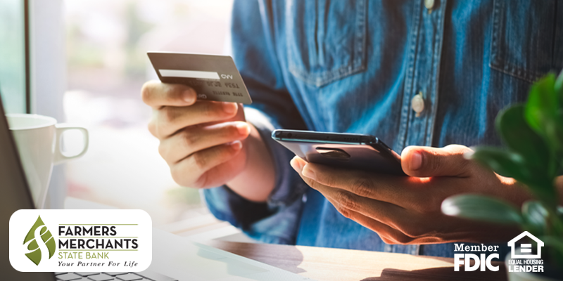 Man seated at table holding smartphone and debit card in hand