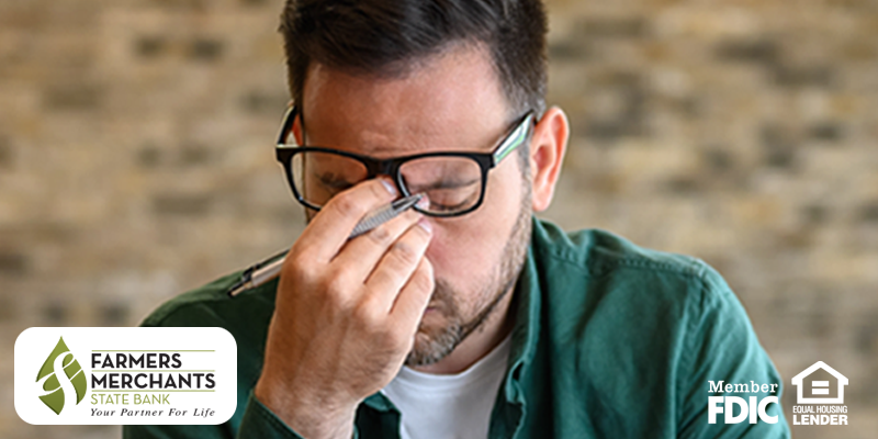 Man wearing glasses with a pen in his hand and his hand pinching the bridge of his nose in stress