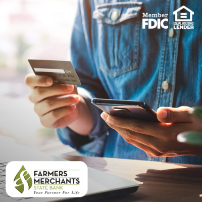 Man seated at table holding smartphone and debit card in hand