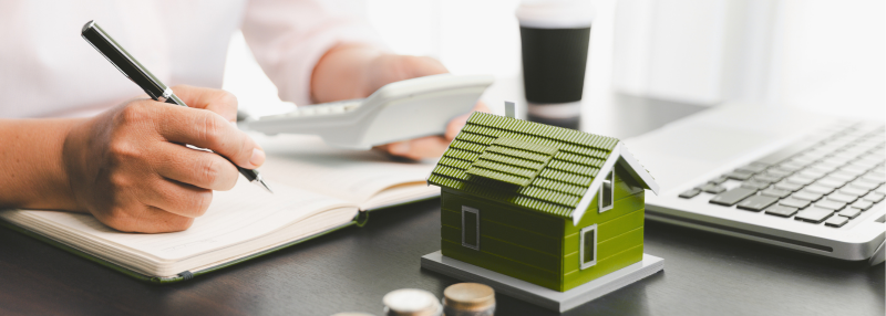 Man at his desk holding a pen and calculator with figure of a house on his desk