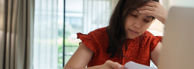 Woman leaning on her hand while looking at documents and her laptop