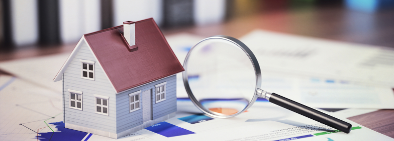 Small model of a home with a magnifying glass next to it on top of papers