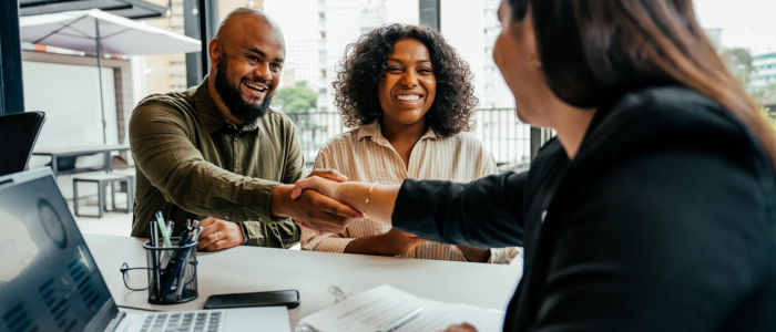 Couple closing on a real state contract with their real estate agent, shaking hands in their office