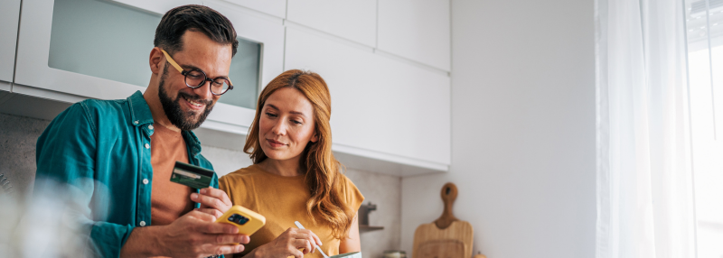 Couple looking at smartphone together while he is holding a debit card in his hand