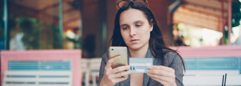 Woman looking at phone while holding credit card in her hand