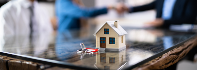 Small house figure with keys and couple shaking hands with lender in the blurred background