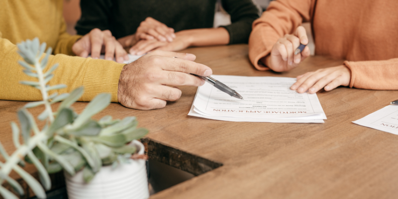 Couple sitting at table with lender and signing loan application