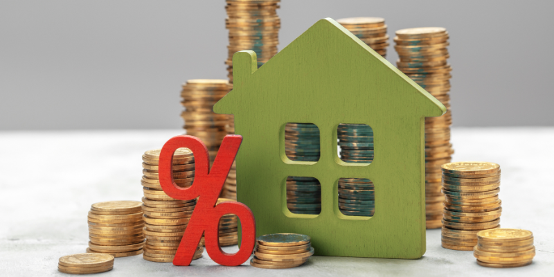 Red percent symbol and green house wooden block with stacks of coins behind them