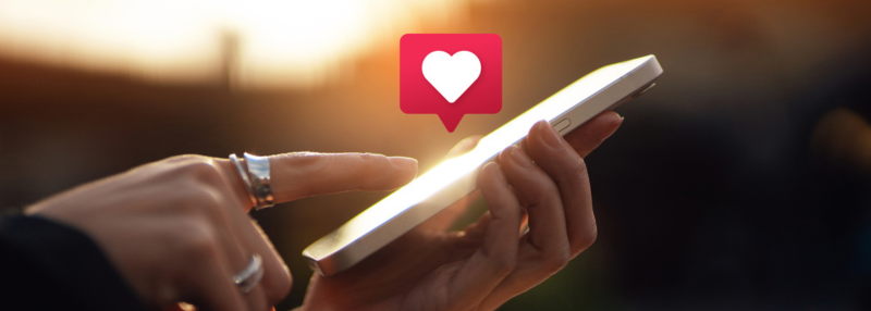 Hand holding phone with icon of heart above it