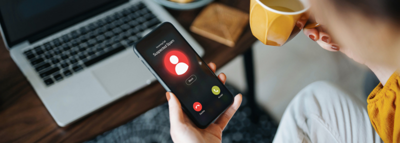 Person holding coffee mug and phone with spam call incoming
